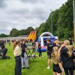 Outdoor community event with kids and volunteers on a grassy field and large inflatable slides in the background.