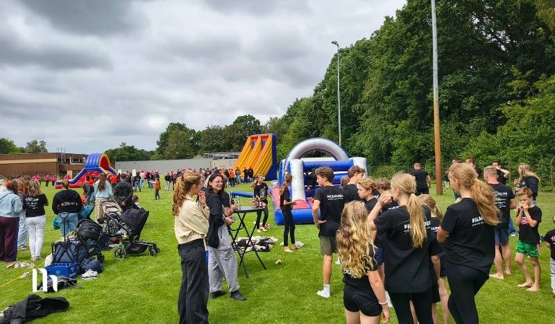 Outdoor community event with kids and volunteers on a grassy field and large inflatable slides in the background.