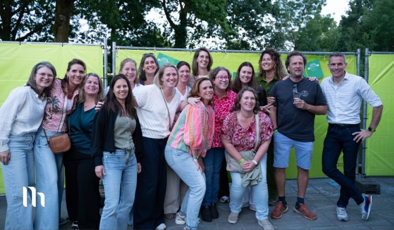 A group of adults posing for a photo at an outdoor event, standing in front of lime-green barriers and smiling at the camera.
